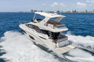 White luxury motor yacht cruising at speed on blue sea, with city skyline in the background.