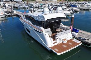 White luxury motor yacht docked at a marina with a spacious rear deck and seating area. Numerous boats line the piers in the background.