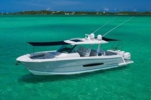 White luxury motor yacht anchored in bright turquoise water with a distant island and blue sky.