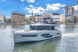 Luxurious yacht moored on calm water with a city skyline and construction cranes in the background under a blue sky