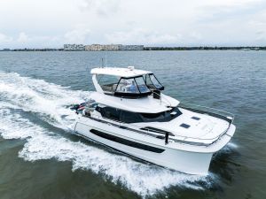 White luxury motor yacht speeds across the water with a distant city skyline and cloudy sky behind it, wake visible in the waves.