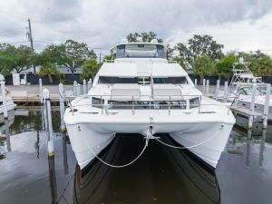 Large white motor yacht docked at a marina with calm water and overcast sky in the background.