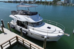 White motorboat moored at a wooden dock along a calm marina with houses across the water.