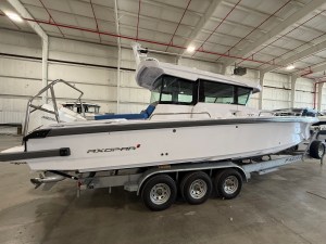 White Axopar motorboat on a multi-axle trailer inside a large indoor storage facility, blue cockpit seating visible.