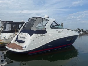 White and navy motor yacht docked at a marina under a partly cloudy sky, name visible on the stern.