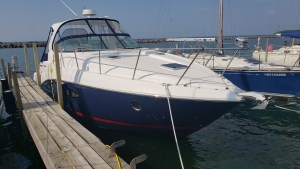 White motor yacht moored at a wooden dock with calm water and clear blue sky in the background.",