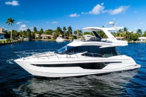 White luxury motor yacht cruising on calm blue water with a palm-lined shore in the background