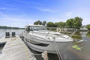 White motorboat moored at a wooden dock on a calm lake, with two lounge chairs on the pier and a clear blue sky above.