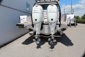 Rear view of a boat with twin white outboard motors and shiny props, parked beside a building.