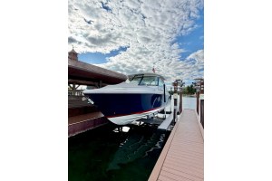 Motorboat moored at a wooden dock with water reflections and a blue, cloudy sky overhead.